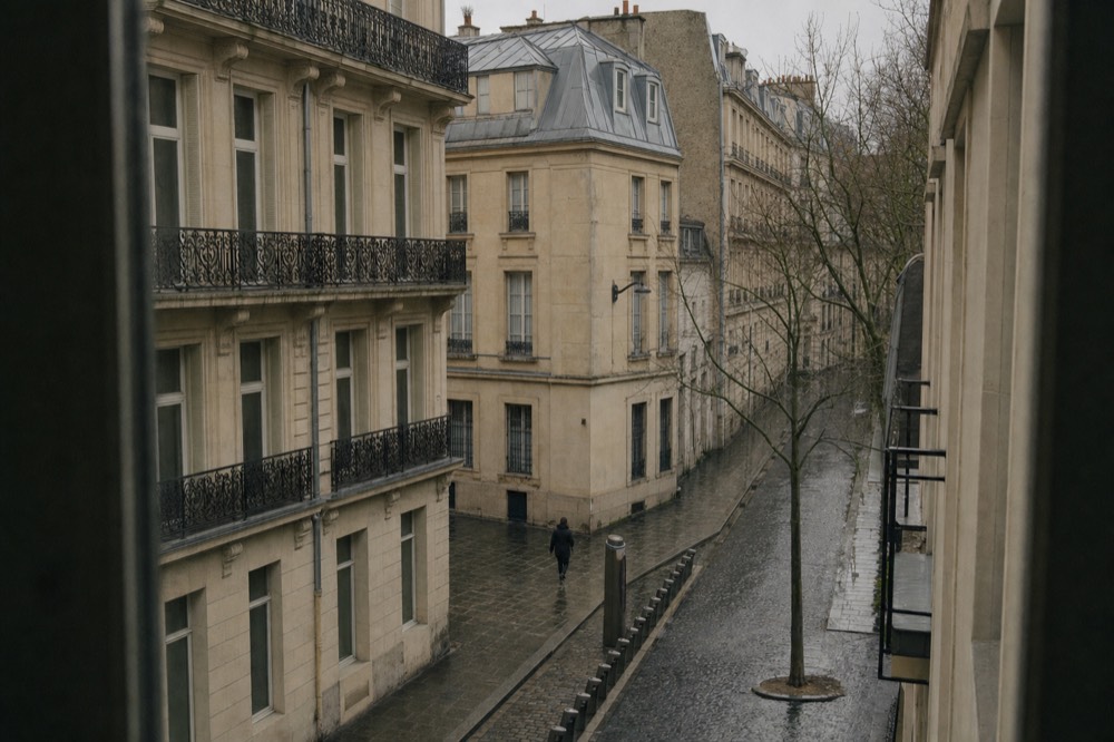 Empty bicycle docking stands line a wet cobbled Paris street below limestone facades and wrought-iron balconies.