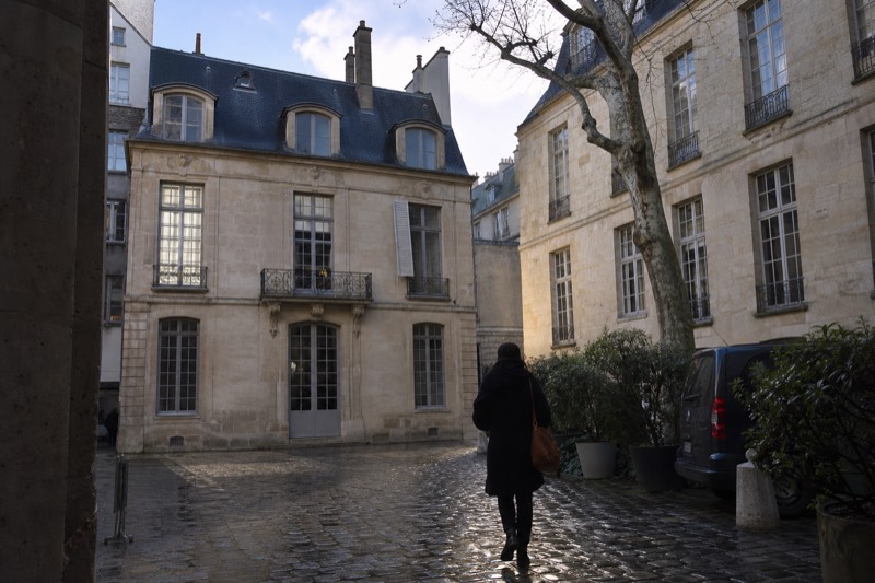 A quiet cobbled courtyard behind a seventeenth century townhouse in Le Marais, pale limestone walls, tall French windows and a bare plane tree in the corner.