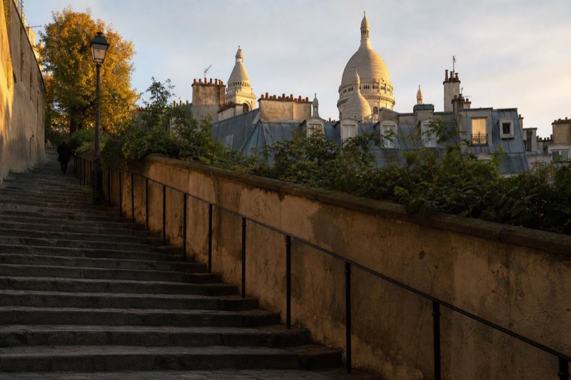 Worn stone steps climb the Montmartre hill in low September evening light, zinc rooftops falling away and the dome of Sacre-Coeur catching the last sun.